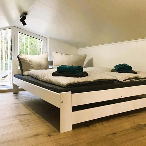 Großes Doppelbett vor einem großen Fenster mit Ausblick in die Natur