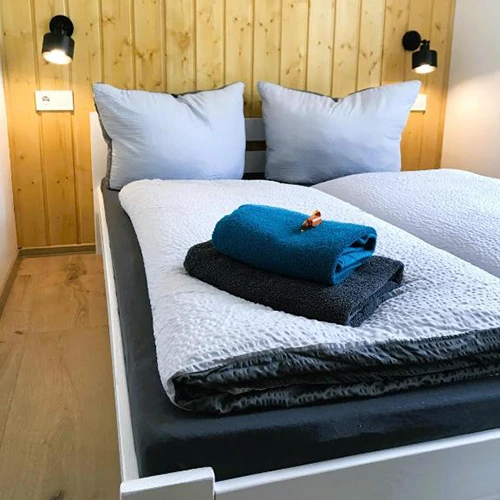 Frisch bezogenes Doppelbett in einem Zimmer mit einer Holzwand